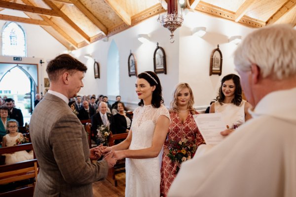 Bride and groom hold hands bridesmaids watch and priest