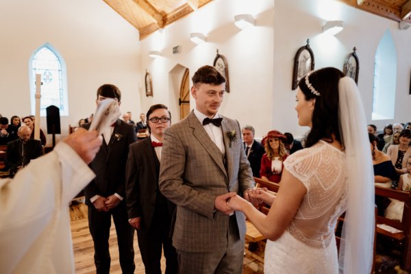 Bride and groom hold hands bridesmaids watch and priest groomsmen