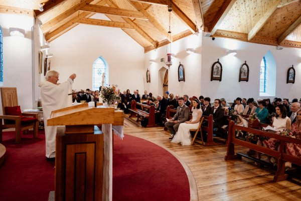 Bride and groom at the alter with priest guests behind