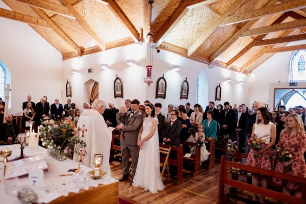 Bride and groom at the alter with priest guests behind