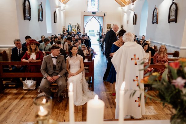 Bride and groom at the alter with priest guests behind