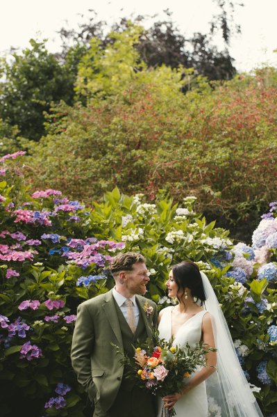 Bride and groom pose in front of flowers in park