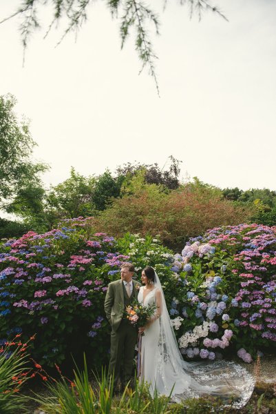 Bride and groom pose in front of flowers in park