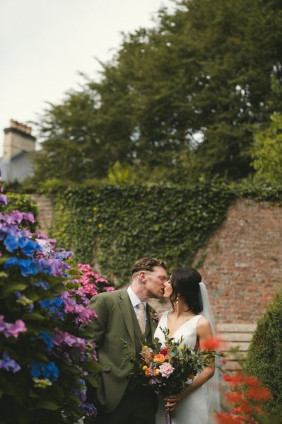 Bride and groom in garden blue and pink flowers kissing kiss