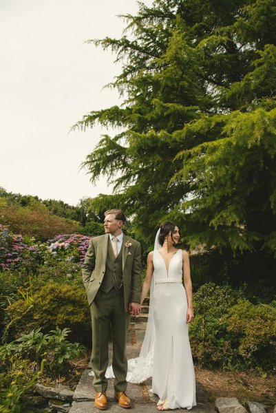 Bride and groom look away hand in hand in garden