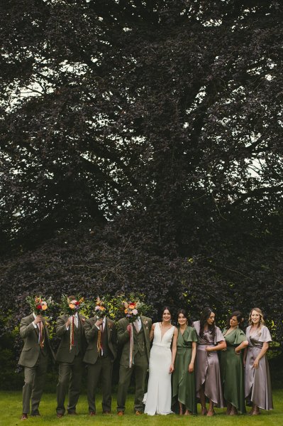 Bride bridesmaids groom and groomsmen pose in park together group shot