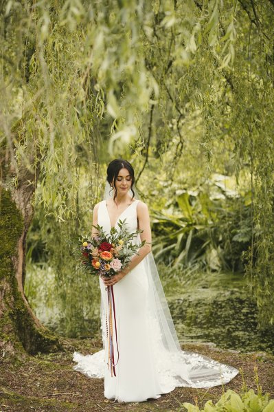 Bride on her own standing in garden surrounded by trees during her Northern Ireland wedding