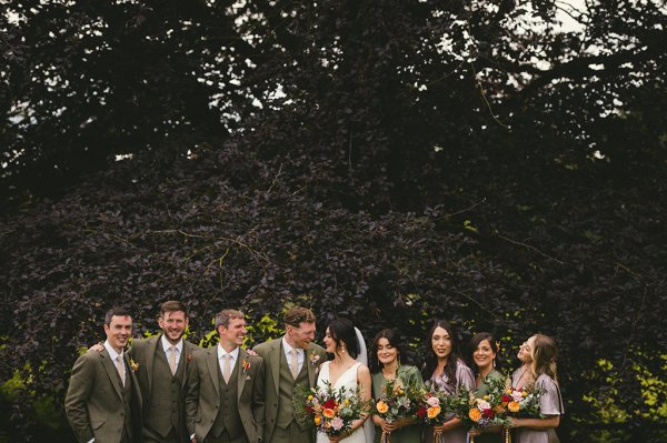 Bride bridesmaids groom and groomsmen pose in park together group shot