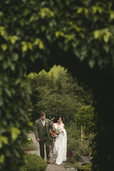 Bride and groom walk hand in hand in garden