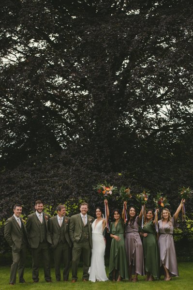 Bride bridesmaids groom and groomsmen pose in park together group shot