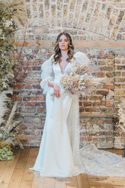 Bride standing in front of bricked wall holding and surrounded by flowers