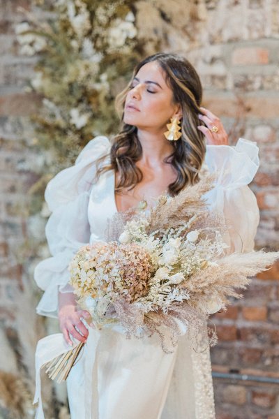 Bride standing in front of bricked wall holding and surrounded by flowers