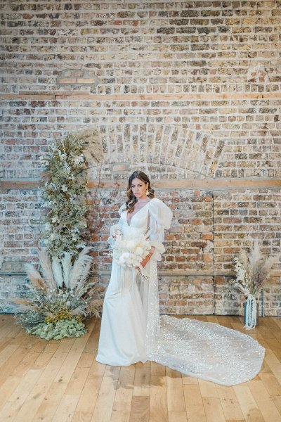 Bride standing in front of bricked wall holding and surrounded by flowers