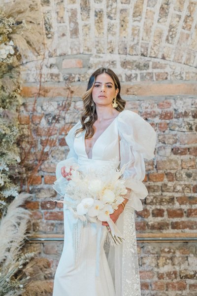 Bride standing in front of bricked wall holding and surrounded by flowers