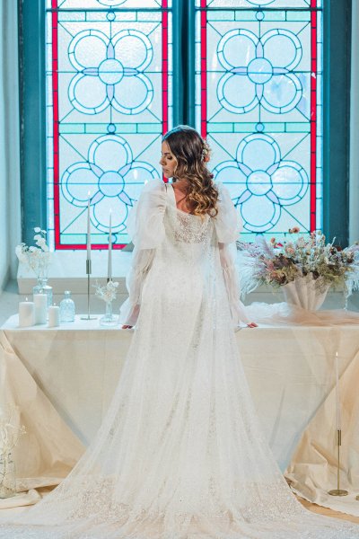 Bride standing at table looking over the shoulder in front of window