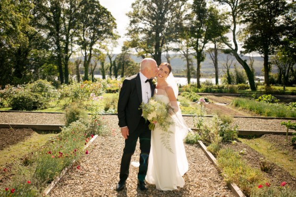 Father of the bride in garden together kiss on the cheek