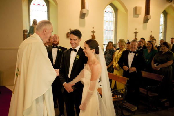 Bride groom priest at alter guests behind