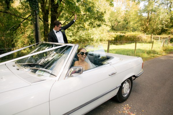 Bride and groom in white wedding car parked in park