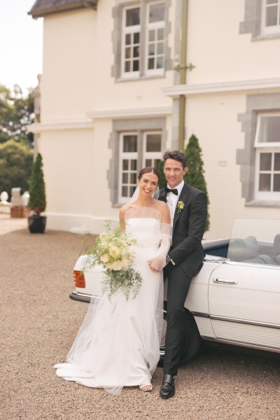 Bride and groom leaning against wedding car