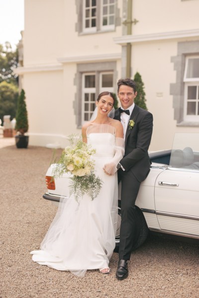 Bride and groom leaning against wedding car