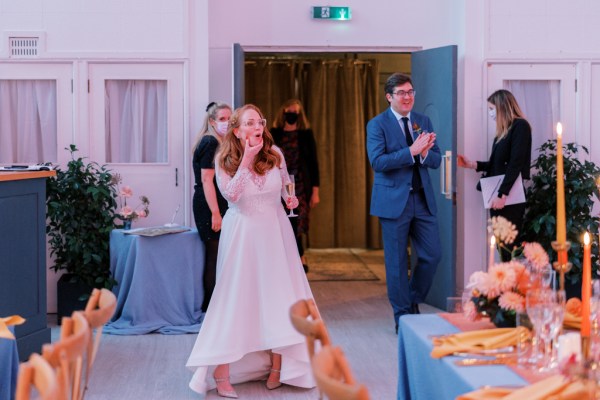 Bride and groom enter dining room clapping smiling at guests