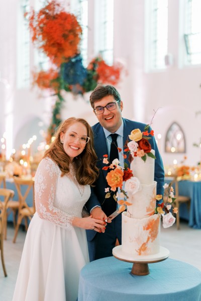 Bride and groom smile whilst cutting the cake colourful flowers