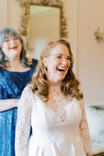 Bride and mother laughing getting ready dress