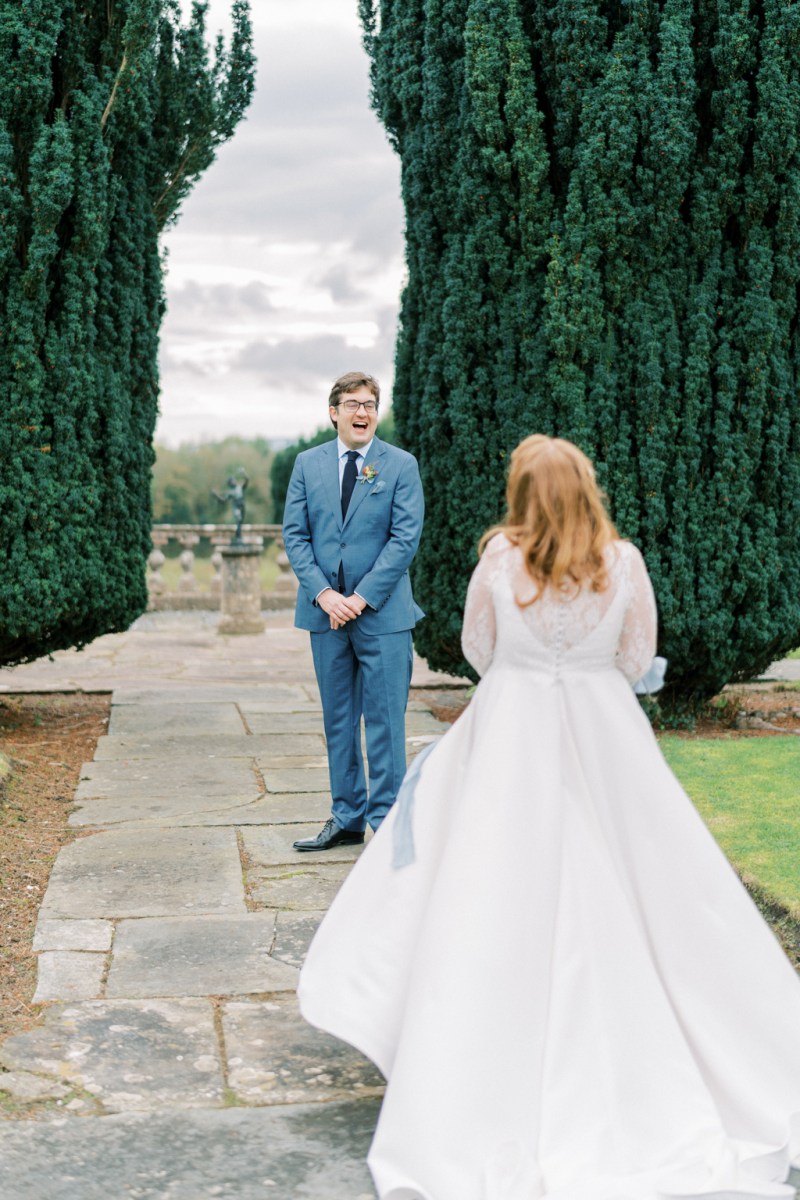 Bride approaches groom embrace holding bouquet in garden