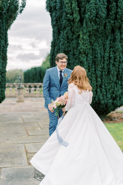 Bride approaches groom embrace holding bouquet in garden