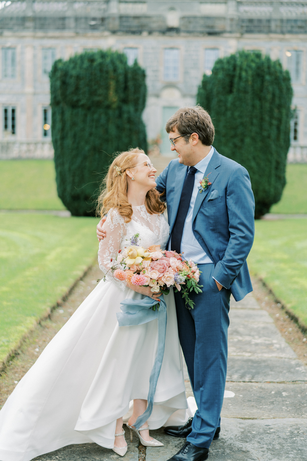 bride and groom stand on pathway in garden holding flowers