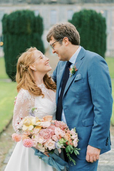 bride and groom stand on pathway in garden holding flowers