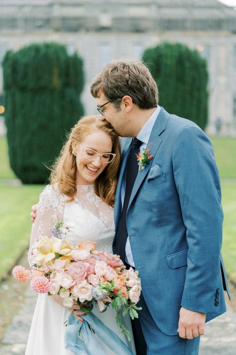 Kiss on the head bride and groom stand on pathway in garden