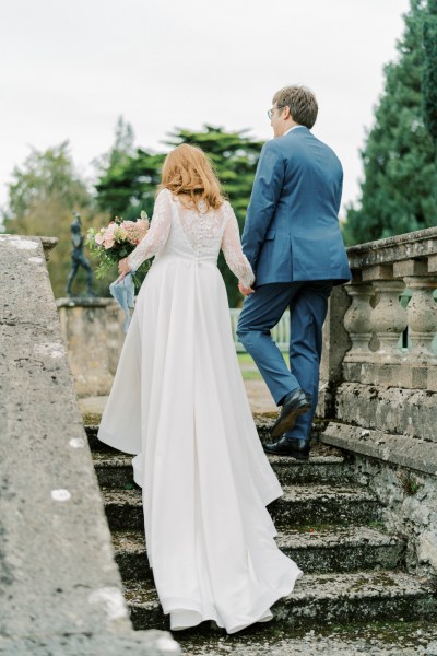 Bride and groom walk up the steps to wedding venue hand in hand