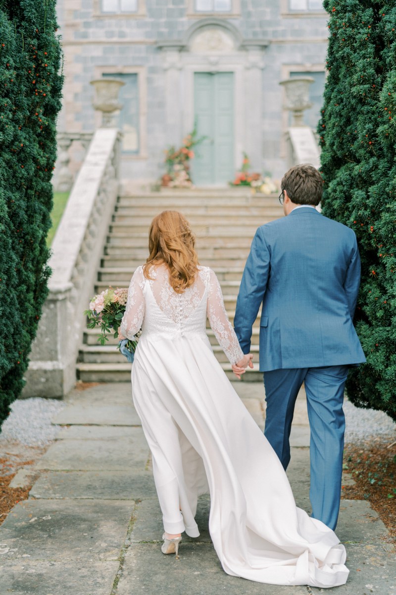 Bride and groom walk up the steps to wedding venue hand in hand