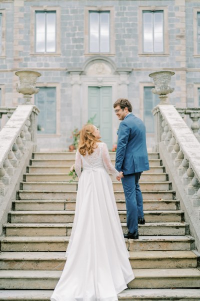 Bride and groom walk up the steps to wedding venue hand in hand