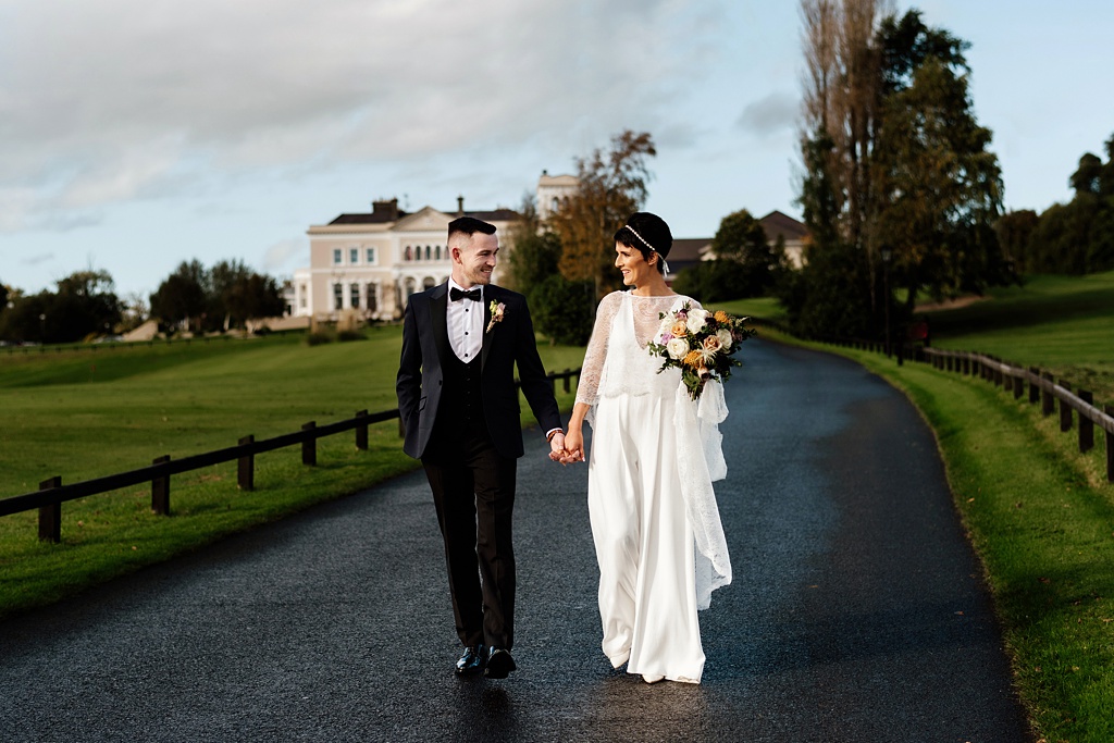 Bride and groom walk along pathway exterior wedding venue