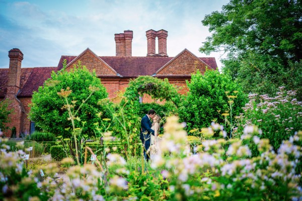 Bride and groom standing in garden flowers surrounding them kissing kiss