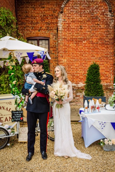 Bride and groom holding baby and flowers in arms hands