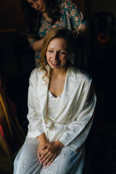 Bride smiles as she gets her hair styled by hairstylist