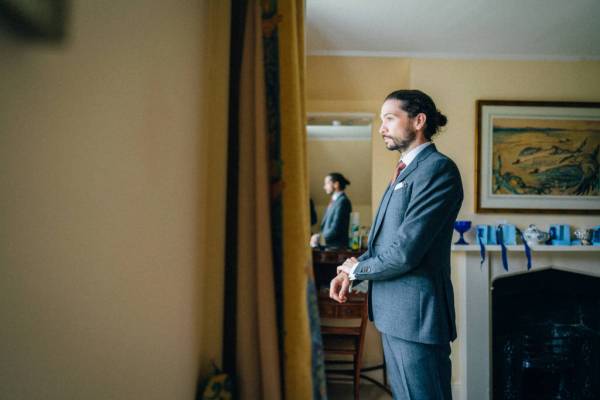 Groom gets ready fixes suit in mirror at window