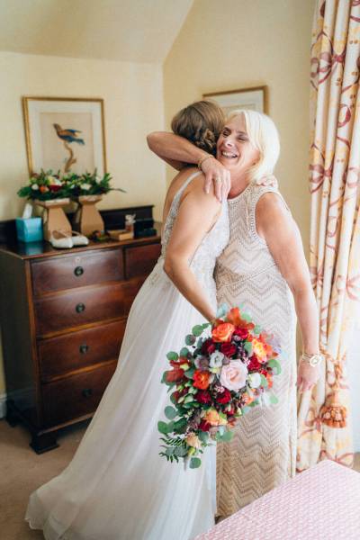 Mother hugs daughter bride holding red pink roses/flowers