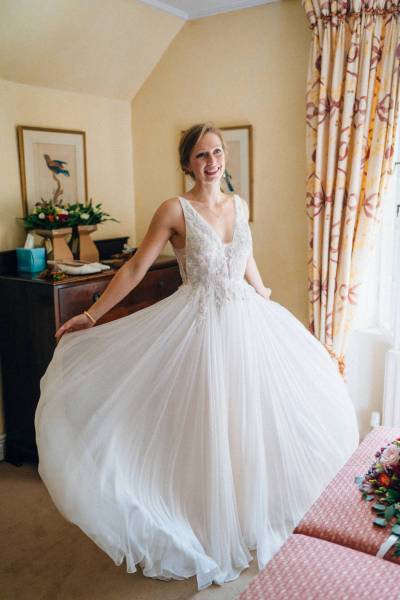 Bride getting ready for wedding showing off dress beside window