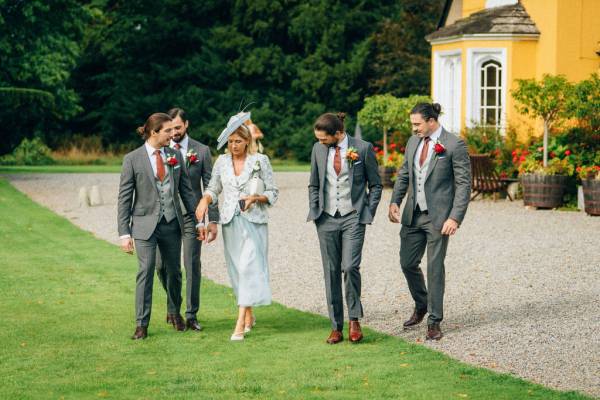 Guests groomsmen mother wearing hat walking on grass