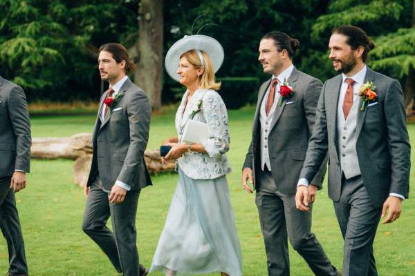 Guests groomsmen mother wearing hat walking on grass