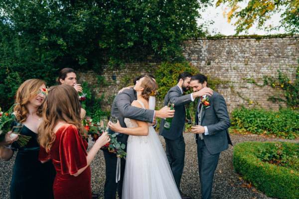 Bride hugs groom groomsmen and bridesmaids holding flowers