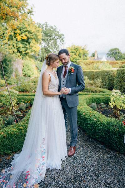 Bride and groom stand in garden bouquet in hand pose for a picture sunny sunshine