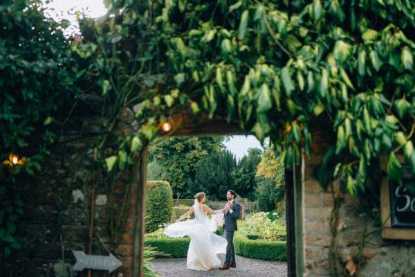 Bride and groom kissing kiss under archway in garden flowers