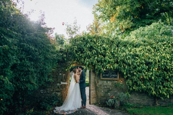 Bride and groom kissing kiss under archway in garden flowers