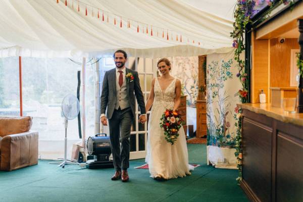 Bride and groom enter ballroom while guests clap for them hand in hand holding hands