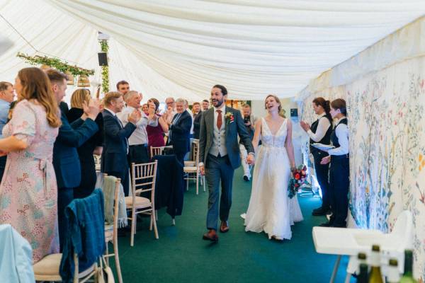 Bride and groom enter ballroom while guests clap for them